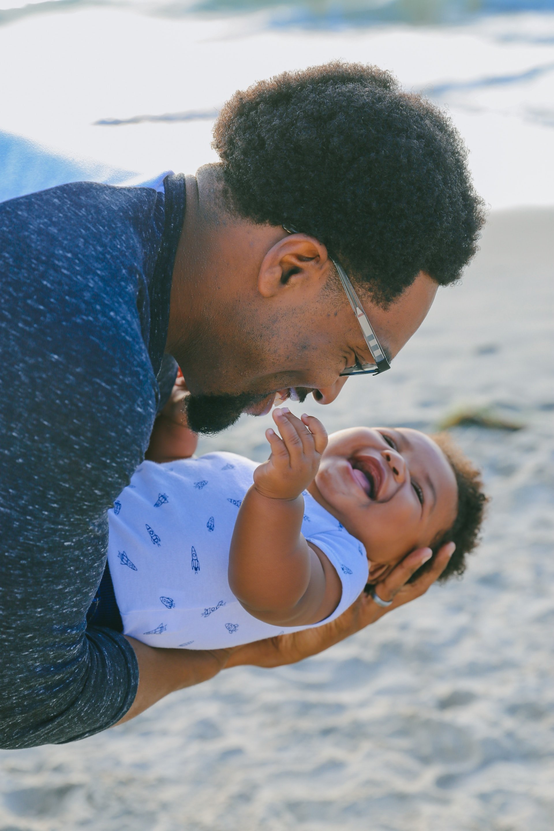 Photo of man holding baby, both laughing.