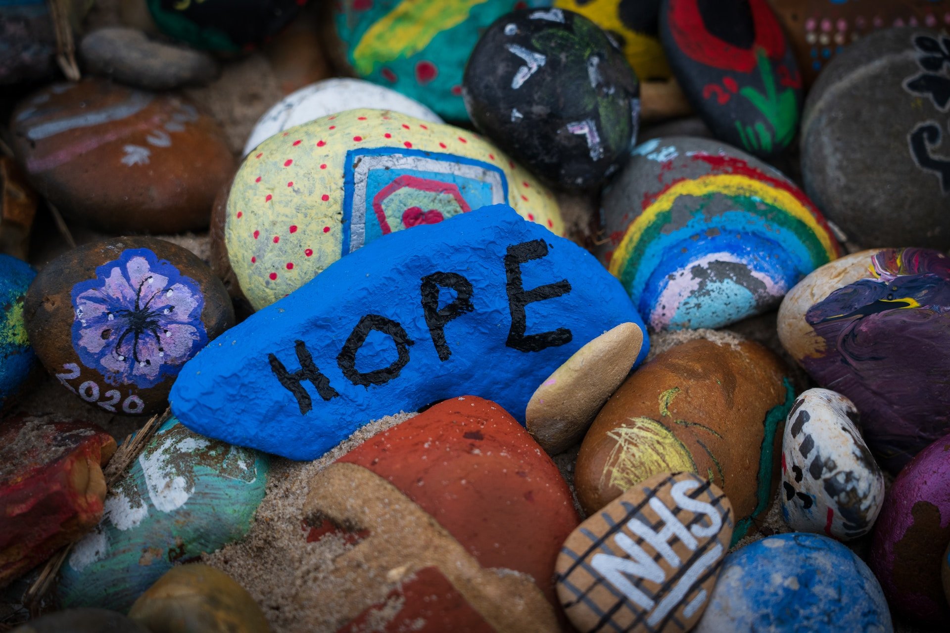 Photo by Nick Fewings on Unsplash: Closeup of colorful painted rocks - blue HOPE rock center.